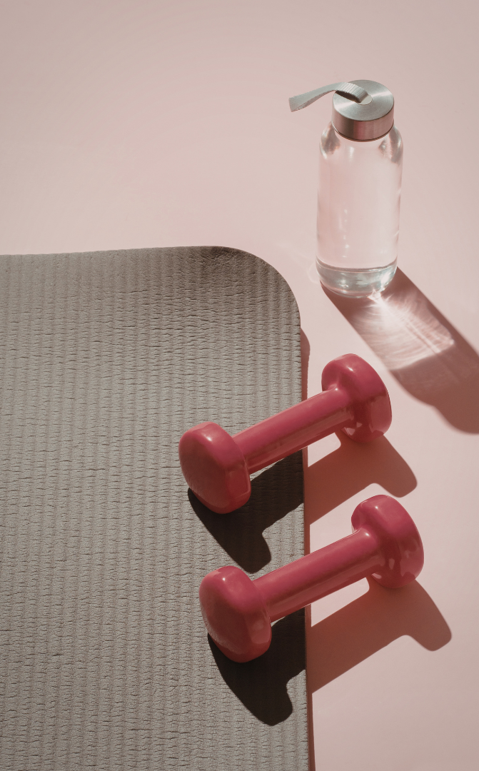 Water bottle placed next to two dumbbells on a pink exercise floor.